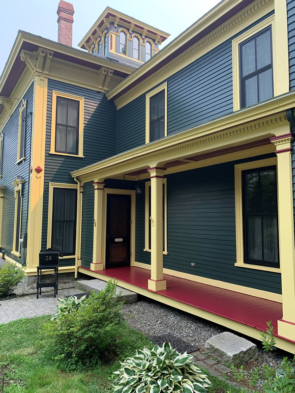 Side view of an historic home painted in dark teal and deep yellow with red accents.